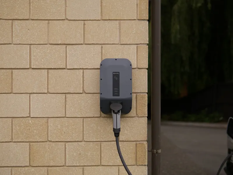 An electric vehicle charger mounted on a brick wall, plugged in
