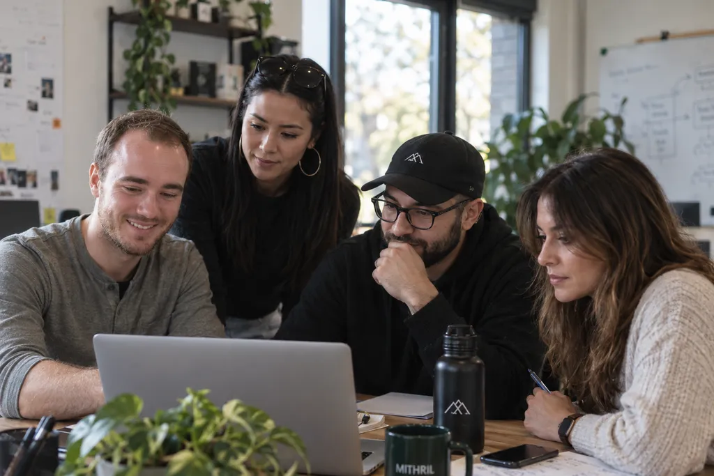 Four people at a work table, gathered around a laptop, a Mithril mug beside it